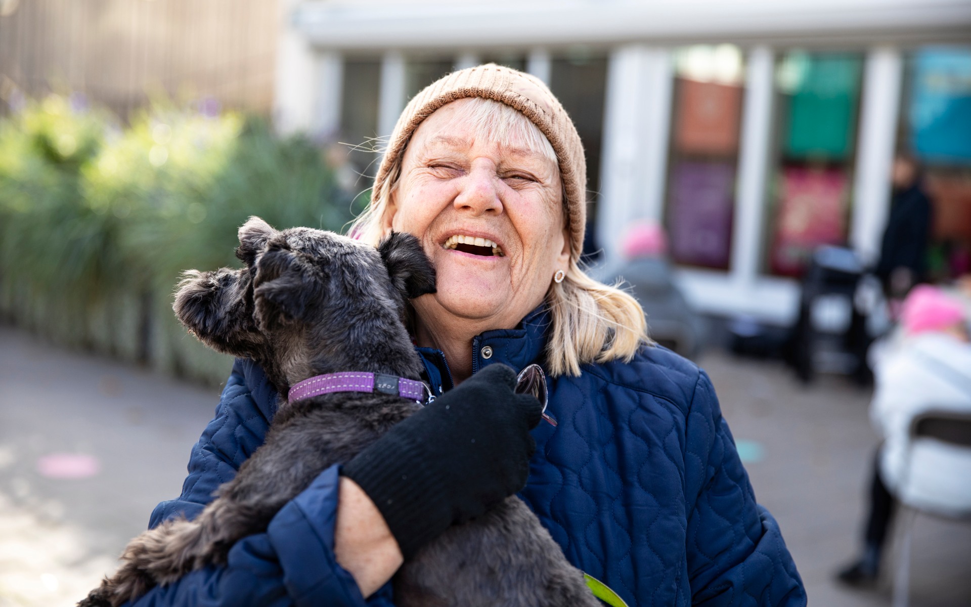 En äldre kvinna skrattar och kramar en svart hund